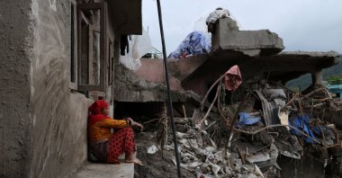 A local day laborer rests outside a flood-damaged house after hanging laundry for an employer in the aftermath of flash floods and mudslides in Devighat, Nuwakot district, Nepal, Sept. 7, 2026. (Reuters Photo)