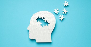 A puzzle shaped like a human head is pictured against a blue background, with several pieces scattered outside the outline, representing memory loss associated with Alzheimer’s disease. (Shutterstock Photo)