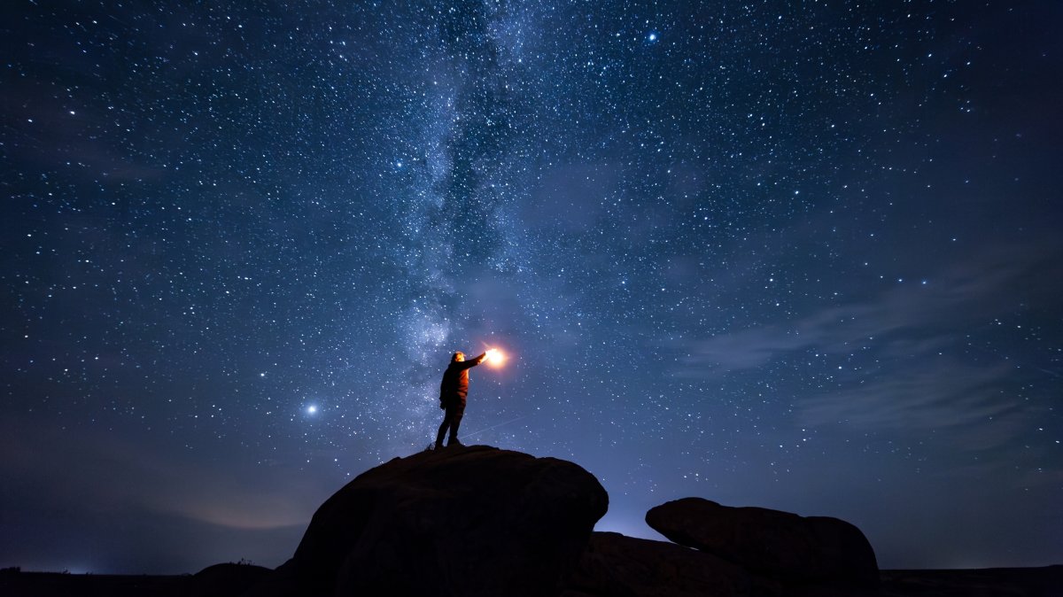 A man holds a lantern while standing atop a stone under a star-filled sky. (Shutterstock Photo)