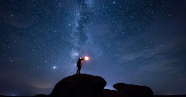 A man holds a lantern while standing atop a stone under a star-filled sky. (Shutterstock Photo)