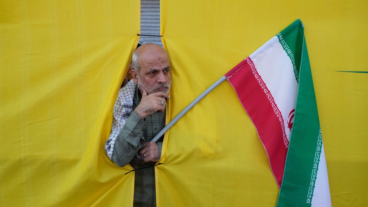 A man holding an Iranian flag peers through an opening in a curtain during the state-organized parade in Tehran, Iran, Sept. 18, 2026. (AP Photo)