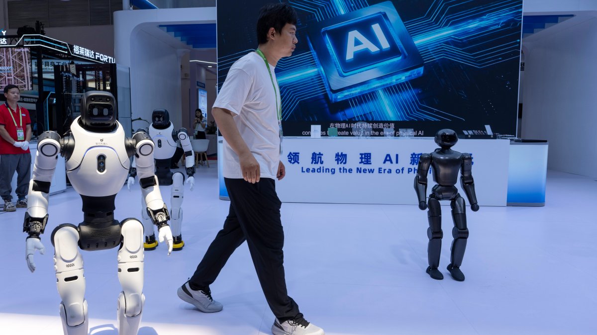 A worker passes by robots from the Chinese company Lens at the China International Supply Chain Expo, Beijing, China, June 22, 2026. (AP Photo)