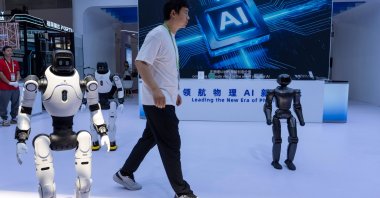 A worker passes by robots from the Chinese company Lens at the China International Supply Chain Expo, Beijing, China, June 22, 2026. (AP Photo)