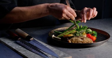 A professional chef meticulously plating a gourmet grilled fish dish with fresh seasonal vegetables using culinary tweezers. (Shutterstock Photo)