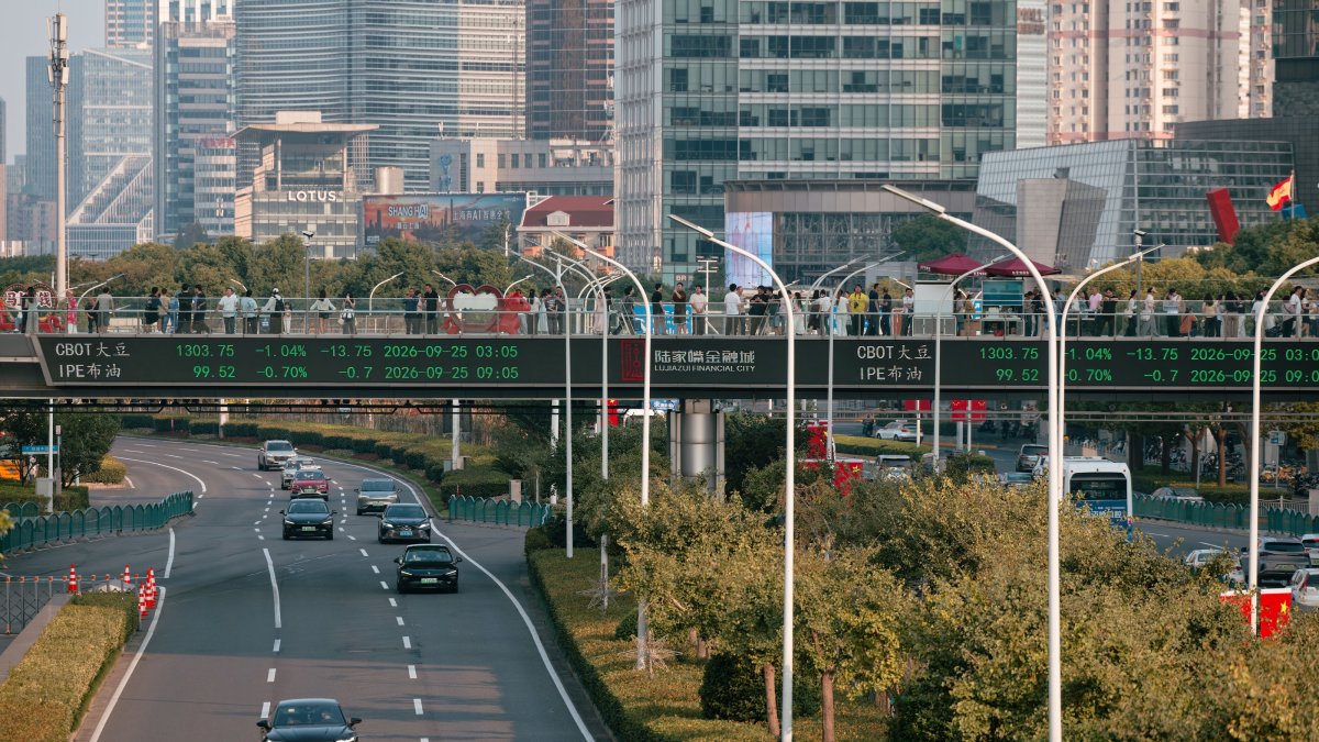 People walk across a pedestrian bridge with a screen showing the latest stock exchange and economic data, Shanghai, China, Sept. 25, 2026. (EPA Photo)