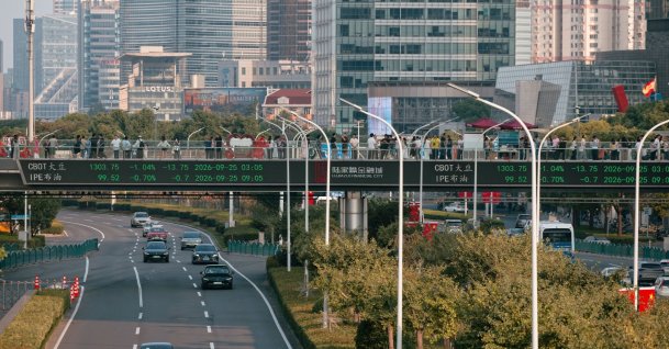People walk across a pedestrian bridge with a screen showing the latest stock exchange and economic data, Shanghai, China, Sept. 25, 2026. (EPA Photo)