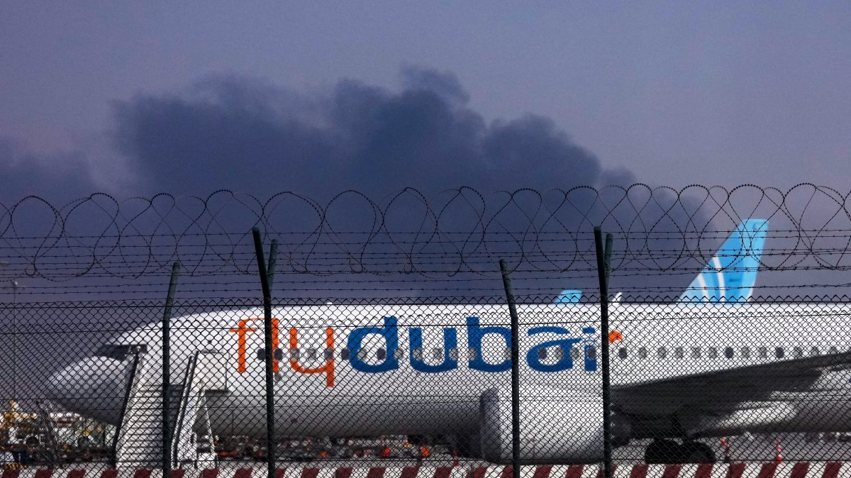 A FlyDubai plane is parked at Dubai International Airport as smoke rises in the background after a drone struck a fuel tank early in the morning, forcing the temporary suspension of flights, Dubai, UAE, March 16, 2026. (AP Photo)