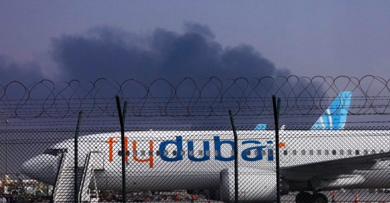 A FlyDubai plane is parked at Dubai International Airport as smoke rises in the background after a drone struck a fuel tank early in the morning, forcing the temporary suspension of flights, Dubai, UAE, March 16, 2026. (AP Photo)