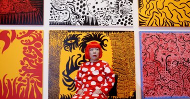Japanese artist Yayoi Kusama poses for photographers in front of her painting "Love Arrives at the Earth Carrying with it a Tale of the Cosmos," center bottom, and other paintings at the Tate Modern, London, U.K., Feb. 7, 2012. (AP Photo)