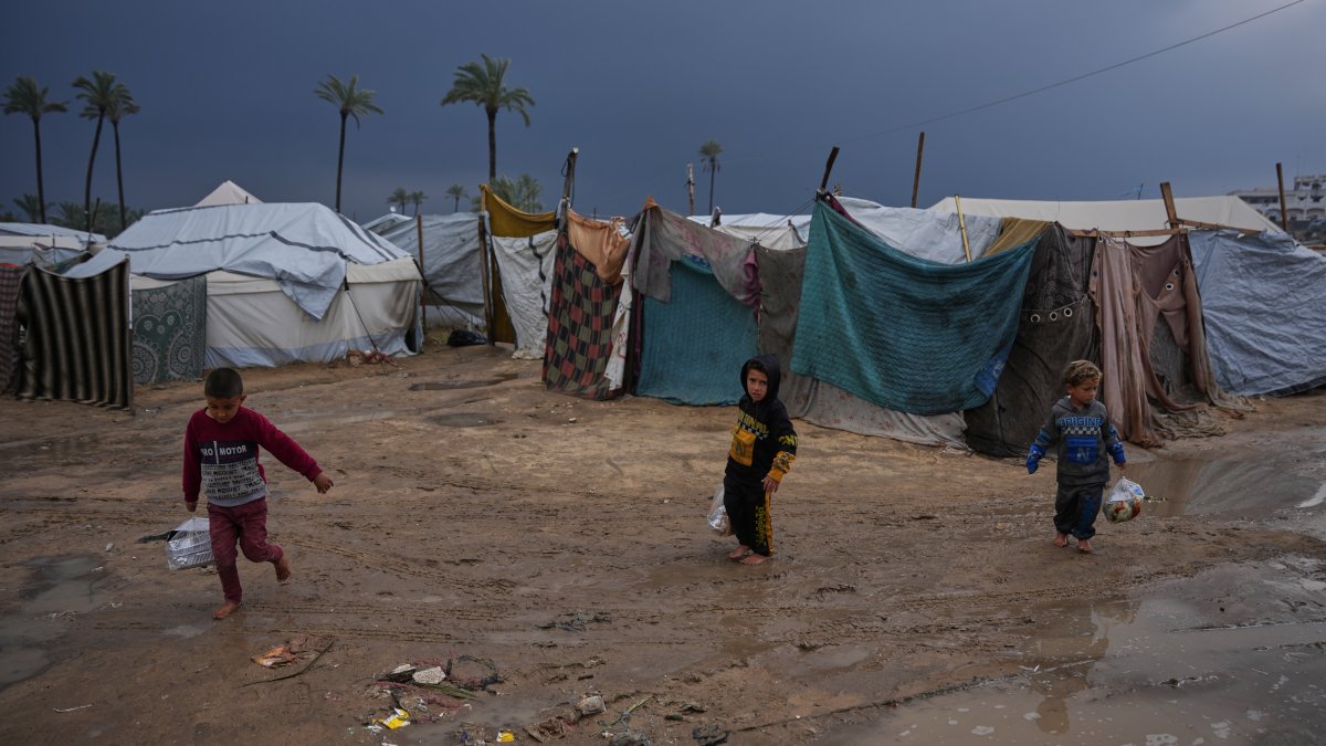 This file photo shows displaced Palestinian children walking through a rain-soaked tent camp following heavy rainfall in Deir al-Balah, central Gaza Strip, Palestine, Feb. 24, 2026. (AP Photo)