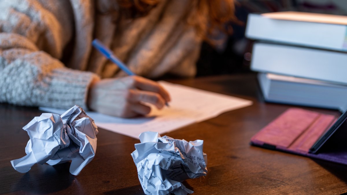 A student studies at a desk surrounded by crumpled sheets of paper. (Shutterstock Photo)