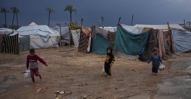 This file photo shows displaced Palestinian children walking through a rain-soaked tent camp following heavy rainfall in Deir al-Balah, central Gaza Strip, Palestine, Feb. 24, 2026. (AP Photo)