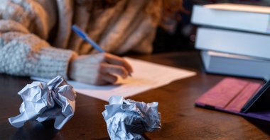A student studies at a desk surrounded by crumpled sheets of paper. (Shutterstock Photo)