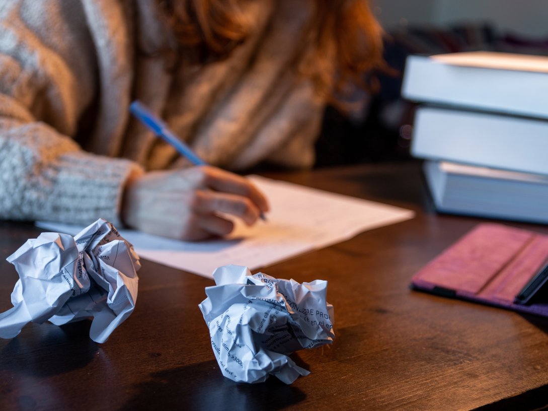 A student studies at a desk surrounded by crumpled sheets of paper. (Shutterstock Photo)