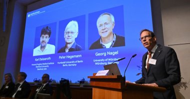 Nobel Committee Secretary-General Thomas Perlmann (R) speaks to the media in front of a screen displaying the names of this year's laureates (L-R) Karl Deisseroth, Peter Hegemann and Georg Nagel during the announcement of the 2026 Nobel Prize in Physiology or Medicine at the Karolinska Institute, Stockholm, Sweden, Oct. 5, 2026. (AFP Photo)