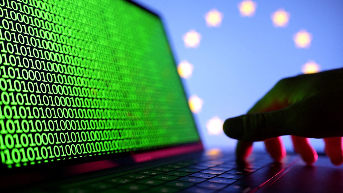A hand is seen on a laptop with binary code displayed in front of the EU flag in this illustration, created on Aug. 19, 2022. (Reuters Photo)