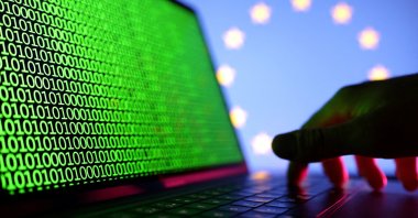 A hand is seen on a laptop with binary code displayed in front of the EU flag in this illustration, created on Aug. 19, 2022. (Reuters Photo)