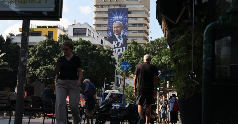 People walk past an election billboard showing Israeli Prime Minister Benjamin Netanyahu with the Hebrew phrase 'We will not surrender' in Tel Aviv, Israel, Oct. 6, 2026. (EPA Photo)