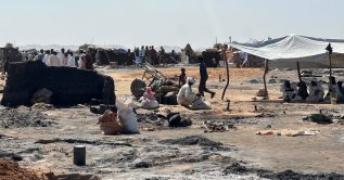 Displaced Sudanese people who left El-Fasher after its fall sit in the shade in Tawila amid the remains of a fire that broke out in the camp on Feb. 11, 2026. (AFP File Photo)