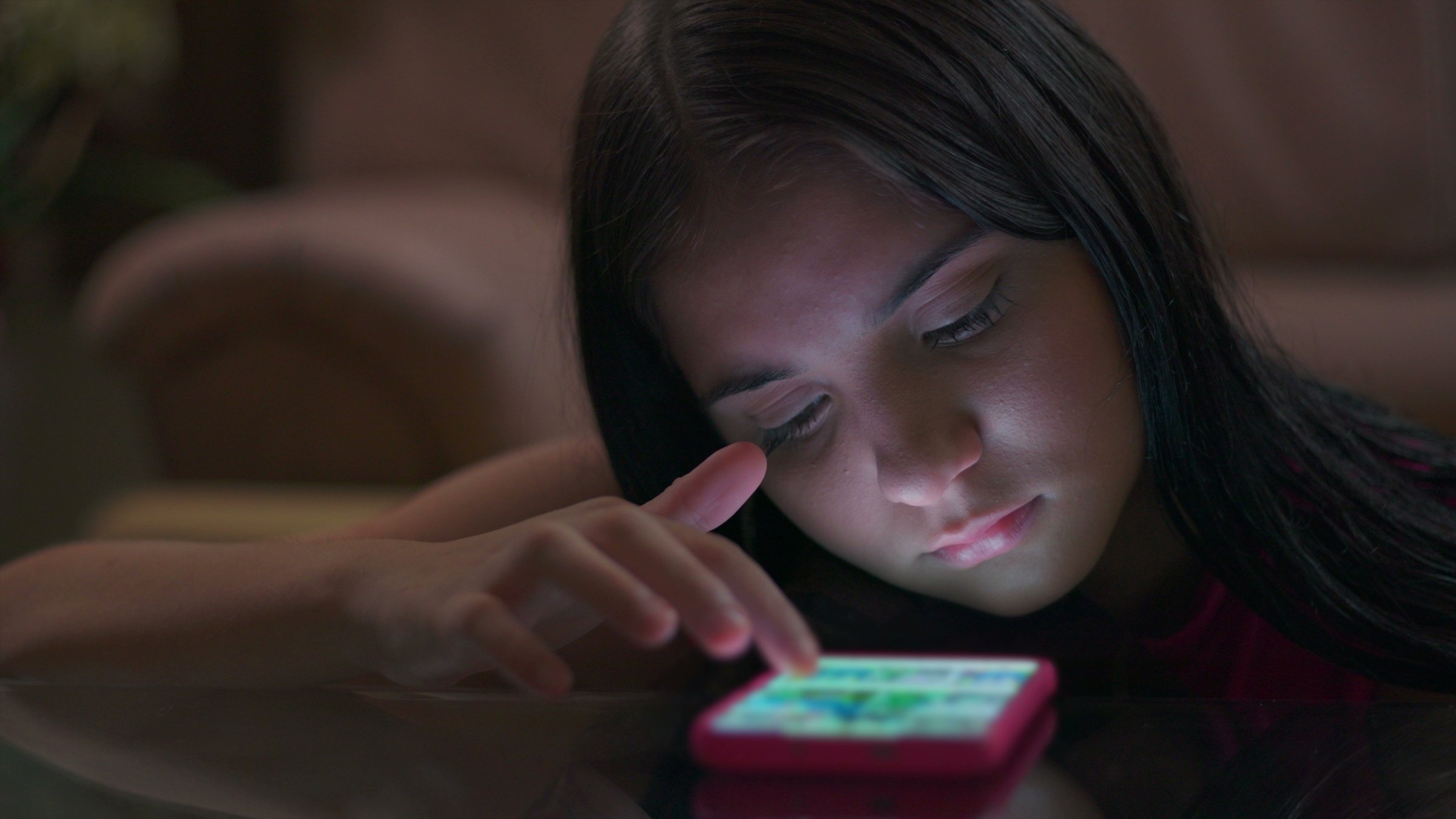Teenage girl at a table engrossed in her phone, with glowing light illuminating her face, illustrating youth caught in social media addiction and tech disconnection. (Shutterstock Photo)
