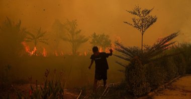 A resident walks as a wildfire burns near a residential area in Banyuasin, South Sumatra province, Indonesia, Oct. 7, 2026. (Reuters Photo)