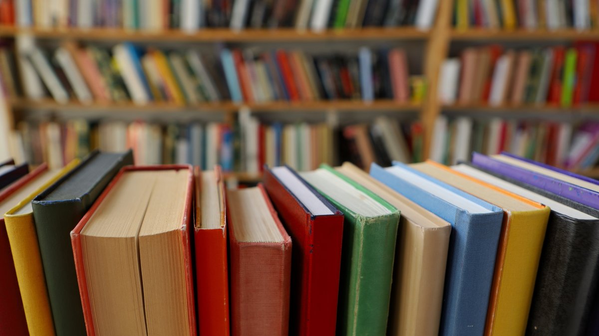 Books are seen on a library shelf, with more books in the background. (Shutterstock Photo)
