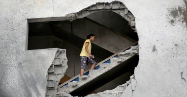 A woman is seen through a gaping hole as she walks up a set of stairs to inspect the site of a house targeted in an Israeli airstrikes in al-Zawayda, central Gaza Strip, Oct. 11, 2026. (AFP Photo)