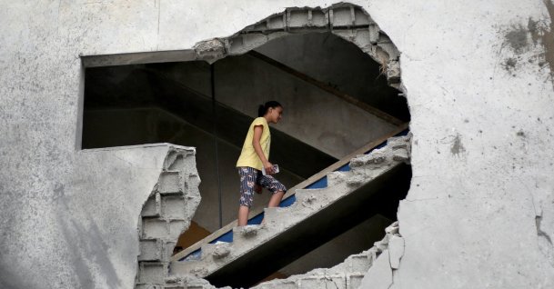 A woman is seen through a gaping hole as she walks up a set of stairs to inspect the site of a house targeted in an Israeli airstrikes in al-Zawayda, central Gaza Strip, Oct. 11, 2026. (AFP Photo)