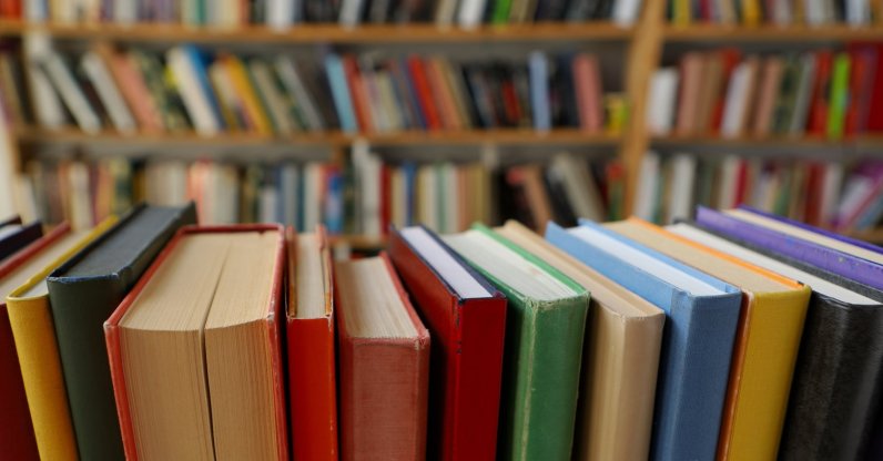 Books are seen on a library shelf, with more books in the background. (Shutterstock Photo)