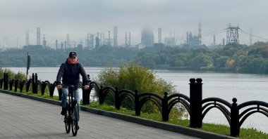 A man rides a bicycle on an embankment of the Moskva River, with the Russian oil producer Gazprom Neft's Moscow oil refinery seen in the distance, on the south-eastern outskirts of Moscow, Russia, Sept. 20, 2026. (AFP Photo)