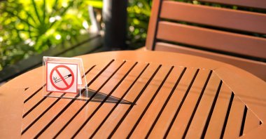 A no-smoking sign sits on a wooden table in a garden. (Shutterstock Photo)