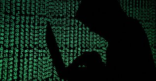 A hooded man holds a laptop computer as cyber code is projected on him in this illustration picture taken on May 13, 2017. (Reuters Photo)