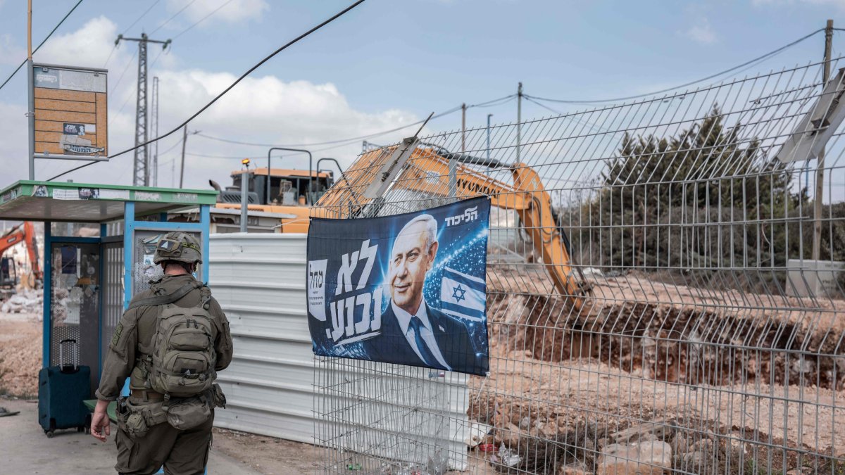 An Israeli soldier walks past a campaign banner of Israeli Prime Minister Benjamin Netanyahu hung along a road in the illegal Israeli settlement of Ofra, occupied West Bank, Oct. 13, 2026. (AFP Photo)
