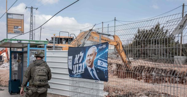 An Israeli soldier walks past a campaign banner of Israeli Prime Minister Benjamin Netanyahu hung along a road in the illegal Israeli settlement of Ofra, occupied West Bank, Oct. 13, 2026. (AFP Photo)