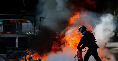 A police officer tries to extinguish a trash can fire during a demonstration to protest against the "high cost of living", Paris, France, Oct. 17, 2026. (AFP Photo)