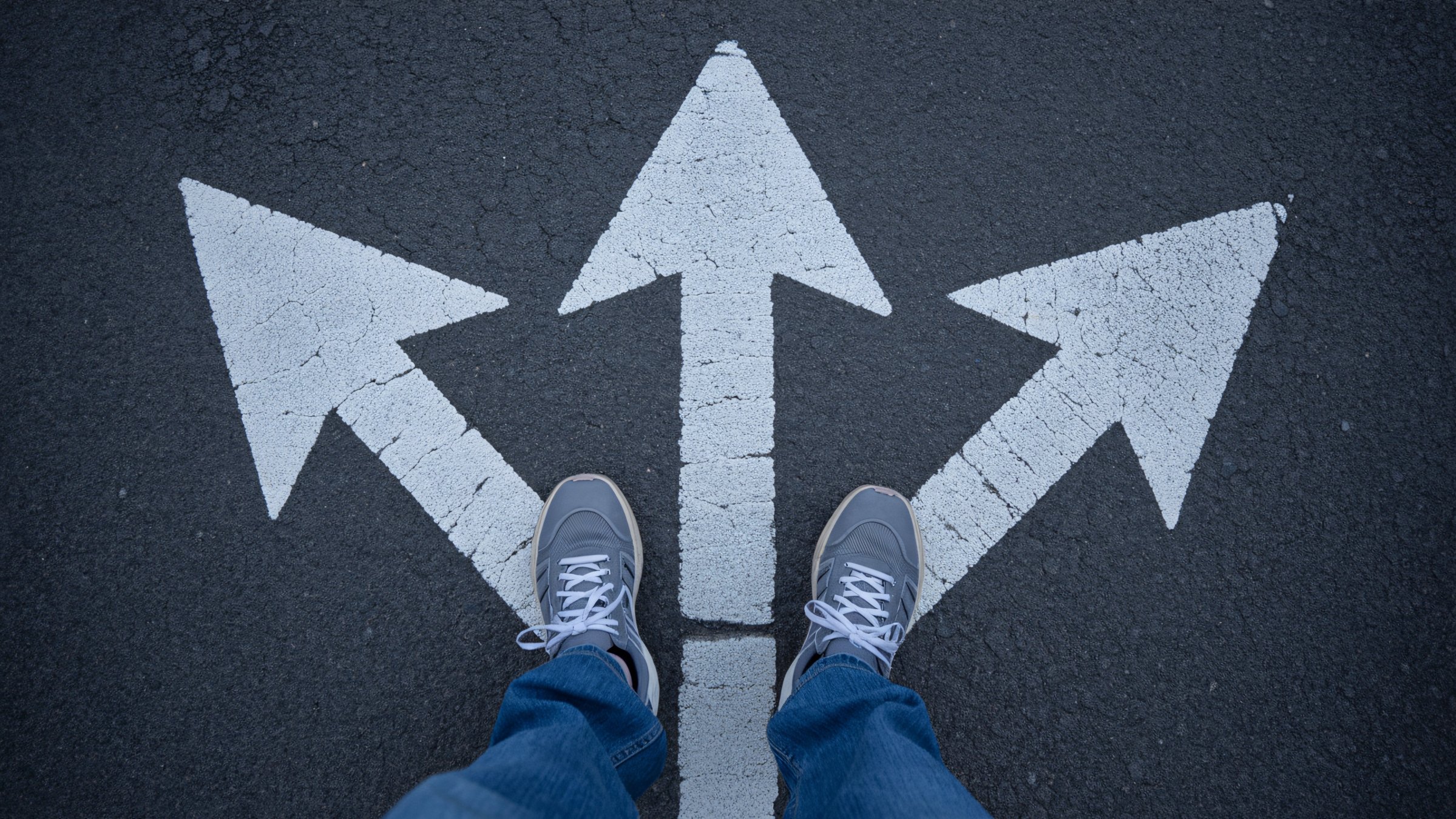 A person stands at a crossroads with multiple arrows pointing in different directions on the ground. (Shutterstock Photo)