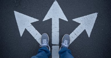 A person stands at a crossroads with multiple arrows pointing in different directions on the ground. (Shutterstock Photo)