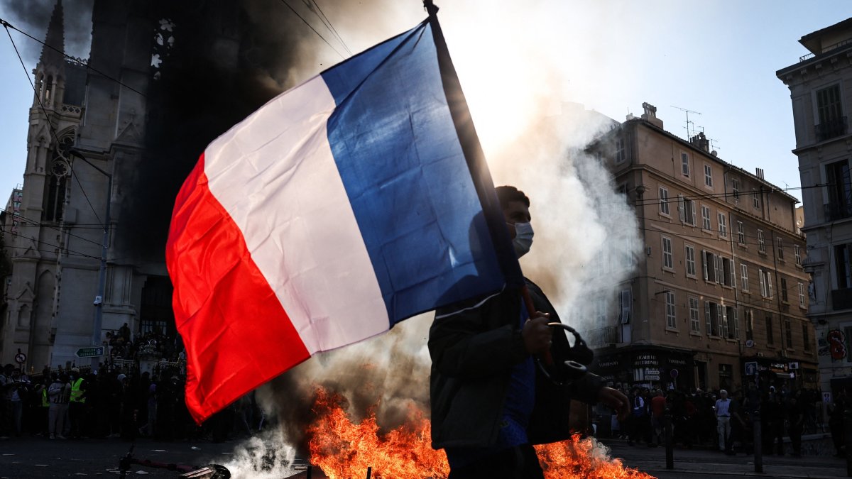 A protester waving a French national flag walks past a fire during clashes prior to the start of a demonstration against the "high cost of living" in Marseille, France, Oct. 17, 2026. (AFP Photo)