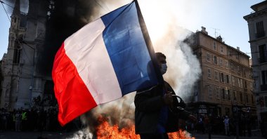 A protester waving a French national flag walks past a fire during clashes prior to the start of a demonstration against the "high cost of living" in Marseille, France, Oct. 17, 2026. (AFP Photo)
