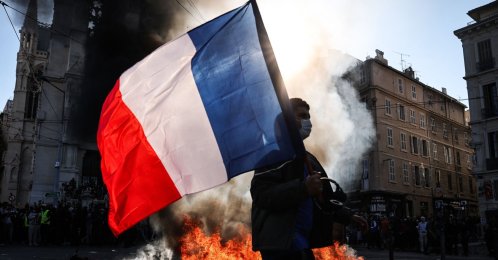 A protester waving a French national flag walks past a fire during clashes prior to the start of a demonstration against the "high cost of living" in Marseille, France, Oct. 17, 2026. (AFP Photo)