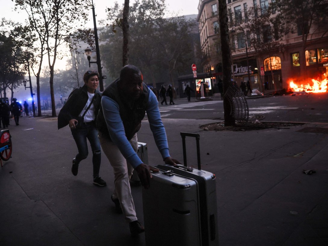 Tourists run with their luggage near Place de La Madeleine and a fire during a demonstration to protest against the "high cost of living" in Paris, France, Oct. 17, 2026. (AFP Photo)