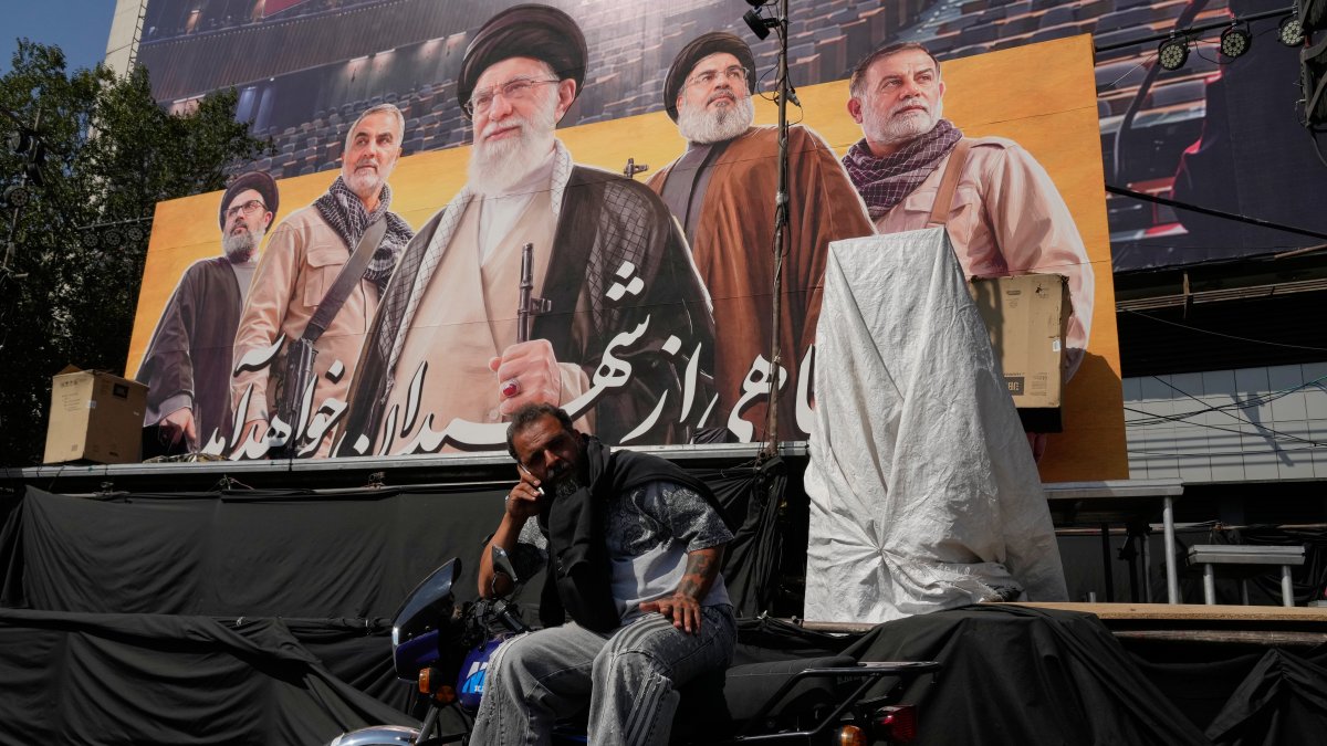 A man talks on his cellphone while sitting on a motorbike in front of a billboard showing portraits of the late Iranian Supreme Leader Ayatollah Ali Khamenei (C) late leaders of Lebanon's Hezbollah group Hassan Nasrallah (2nd R) and Hashem Safieddine (L) late commander of Iran's Revolutionary Guard Quds Force, Gen. Qassem Soleimani (2nd L) and a top commander of the guard Gen. Abbas Nilforoushan, who were killed in Israeli and U.S. strikes, at the Islamic Revolution Square in Tehran, Iran, Oct. 12, 2026. (AP Photo)