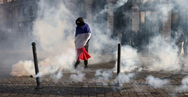 A protester, wrapped in a flag of France, stands in the smoke at Place de l'Opera during ongoing protest action against the "high cost of living", in Lille, northern France, Oct. 17, 2026. (AFP Photo)