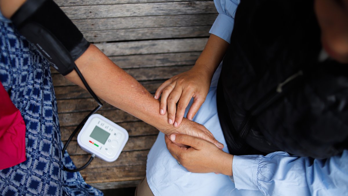 A health care worker checks the blood pressure of an elderly woman in a rural area during a medical visit. (Shutterstock Photo)