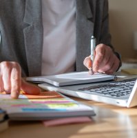 A person takes notes in a notebook while taking an online course. (Shutterstcok Photo)