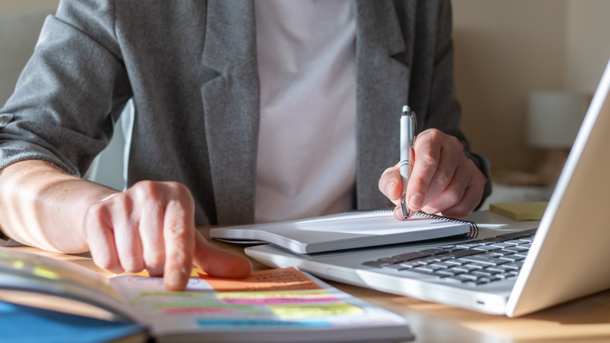 A person takes notes in a notebook while taking an online course. (Shutterstcok Photo)