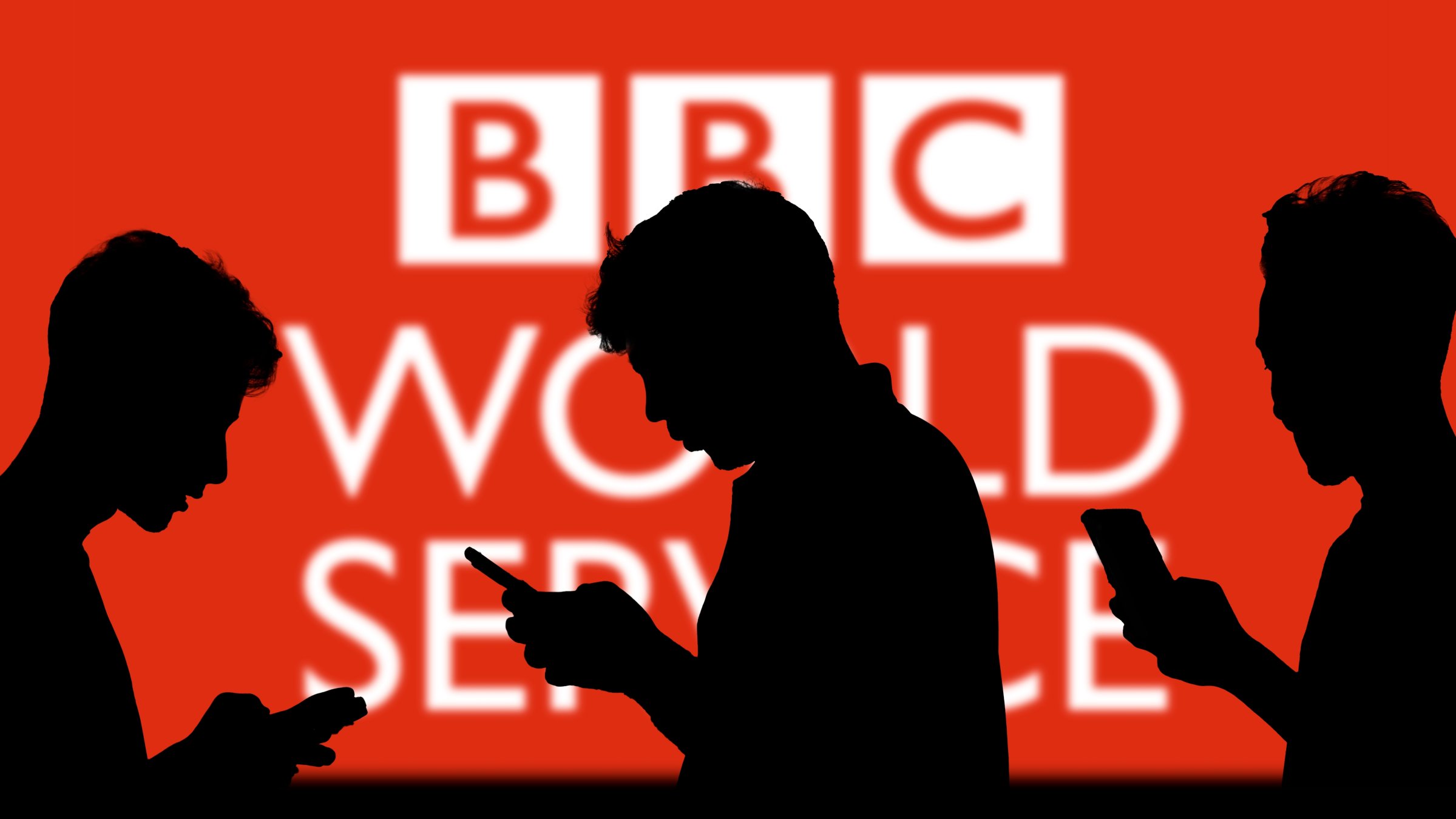 The BBC logo is seen on a screen behind people looking at their smartphones, Dhaka, Bangladesh, Nov. 13, 2024. (Shutterstock Photo)