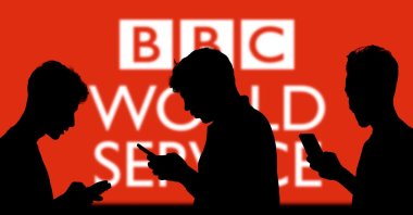 The BBC logo is seen on a screen behind people looking at their smartphones, Dhaka, Bangladesh, Nov. 13, 2024. (Shutterstock Photo)