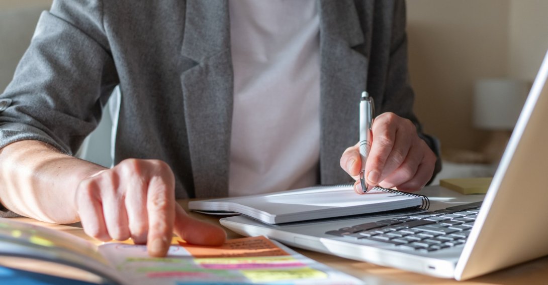 A person takes notes in a notebook while taking an online course. (Shutterstcok Photo)