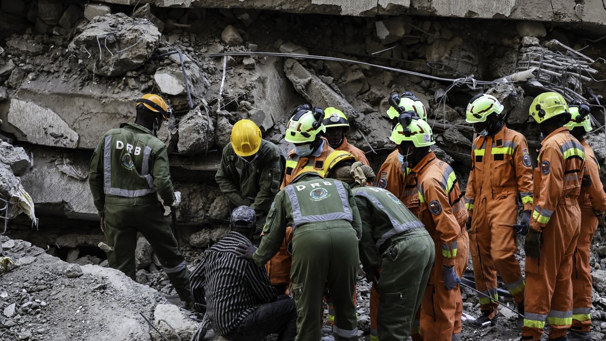 epa13326134 Emergency personnel assist a man (L, seated) who said his wife was trapped under the rubble as search and rescue operations continue at the site of a collapsed multi-story building under construction in the Eastleigh neighborhood of Nairobi, Kenya, 23 October 2026. Rescuers deployed heavy machinery and sniffer dogs to clear debris, with an unconfirmed number of people feared trapped beneath the rubble.  EPA/DANIEL IRUNGU